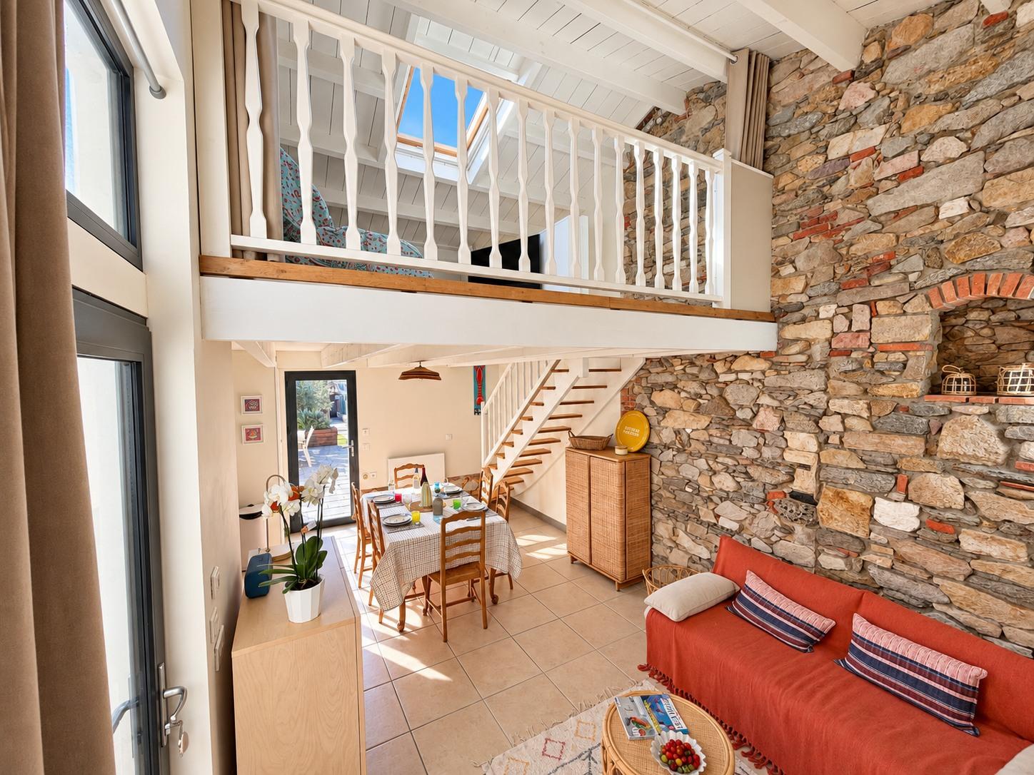 Le séjour vu depuis l'entrée, avec la mezzanine, le mur de pierre et le canapé terracotta